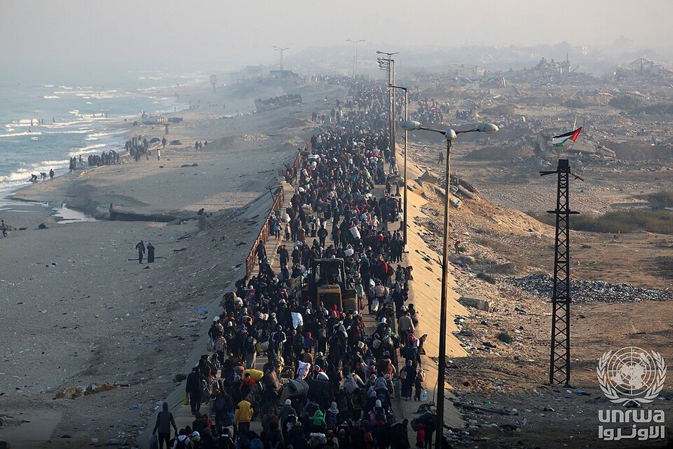 Displaced Palestinians walking along Al-Rasheed Street during their journey back to Gaza, carrying belongings and pushing carts amid ongoing conflict